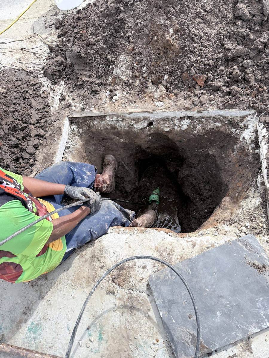 Two G&R technicians examining an exposed sewer line in a trench